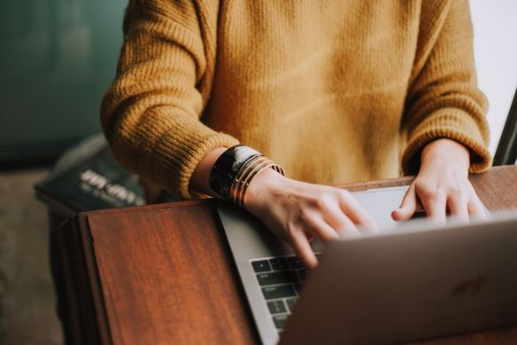 Woman in a yellow sweater at a desk writing a journal entry on her computer